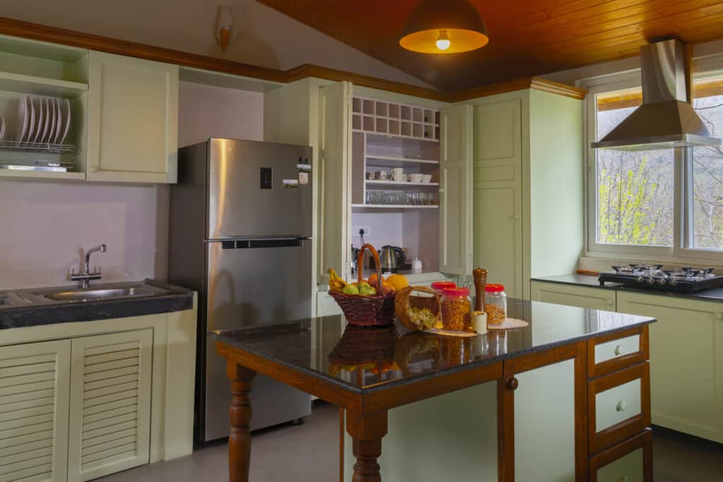 A kitchen with counters and cabinet in green, a refrigerator and a wooden table