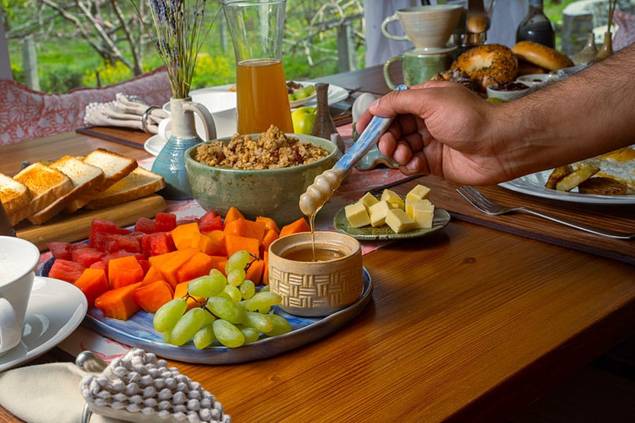 A person enjoying a breakfast of fruit and cereal with honey